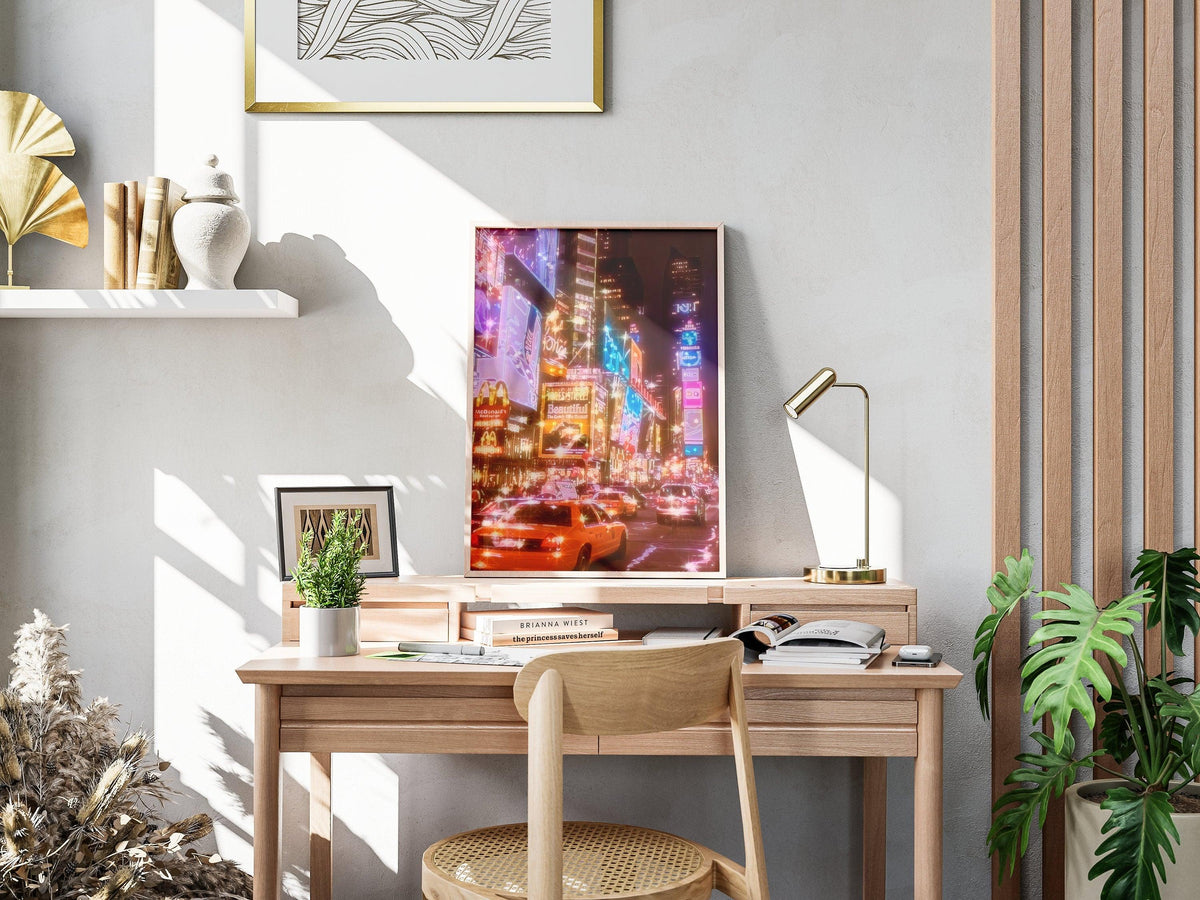 Times Square neon print leaning on a light oak desk beside a brass lamp